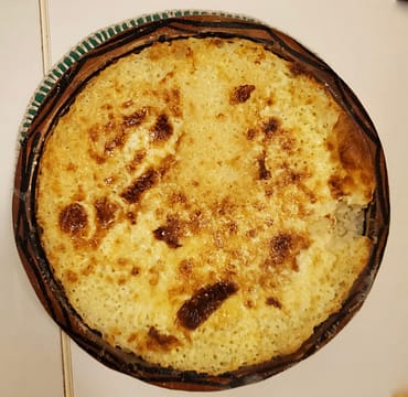 A top-down view of creamy baked rice in a traditional clay pot with a golden-brown, bubbly crust.