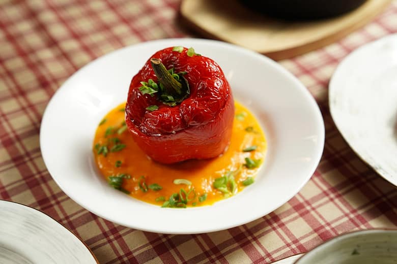 Roasted stuffed red bell pepper served on a plate with sauce and chopped green herbs.