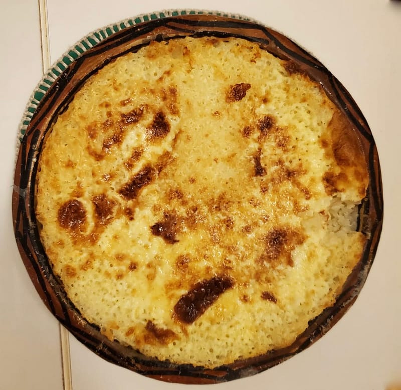 A top-down view of creamy baked rice in a traditional clay pot with a golden-brown, bubbly crust.