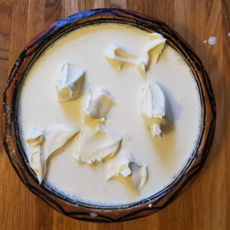 Thick dollops of fresh cream being swirled into a clay pot of milk and rice.